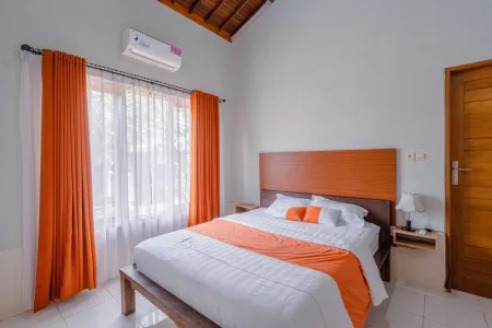 Cozy Balinese bedroom with wooden bed, orange bedding and curtains, air conditioning, and tropical thatched ceiling.
